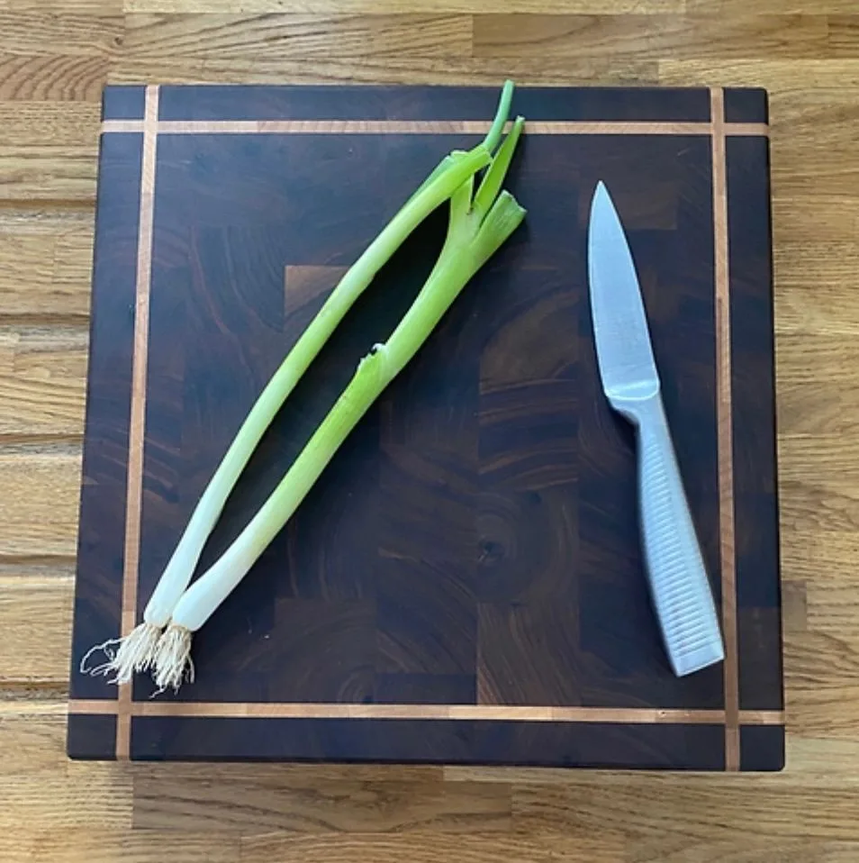 A striped wooden chopping board with a red chilli and a knife on it